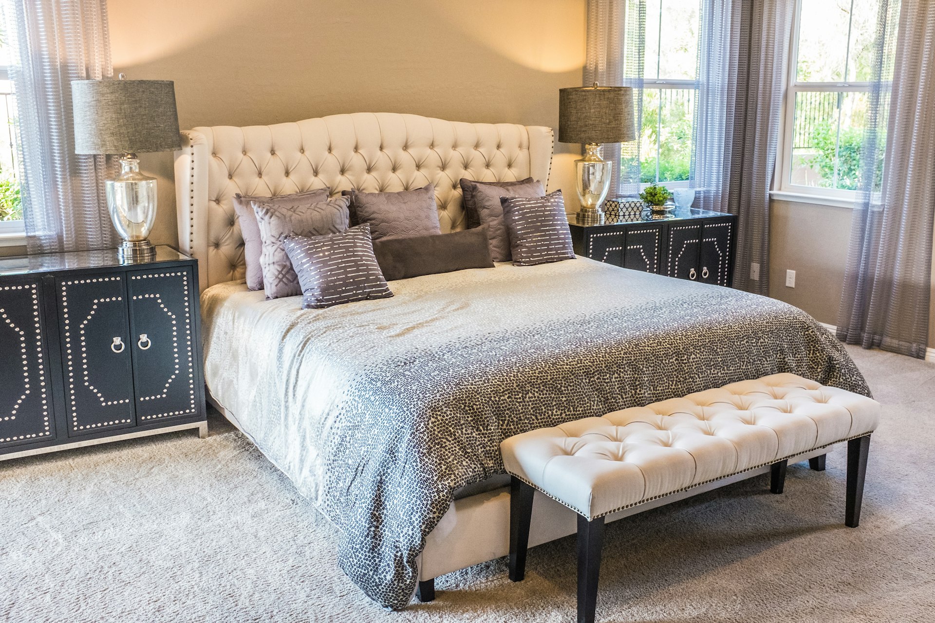 Modern bedroom with tufted headboard, patterned bedding, and sheer curtains in neutral tones